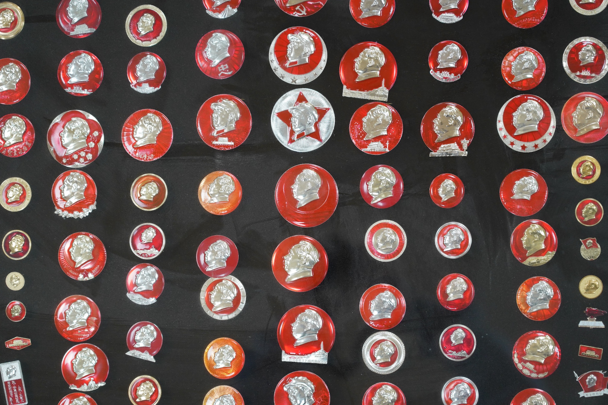 A display case of Chinese red enamelled badges with the head of Chairman Mao, 72 x 85cm